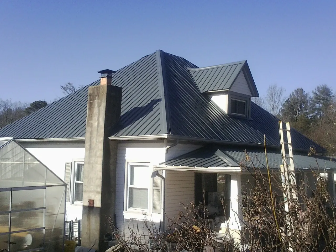 Dark blue standing seam metal roof on a white farmhouse with dormer — Slate & Tile Roof Repair by Roofing Brothers in Dearborn