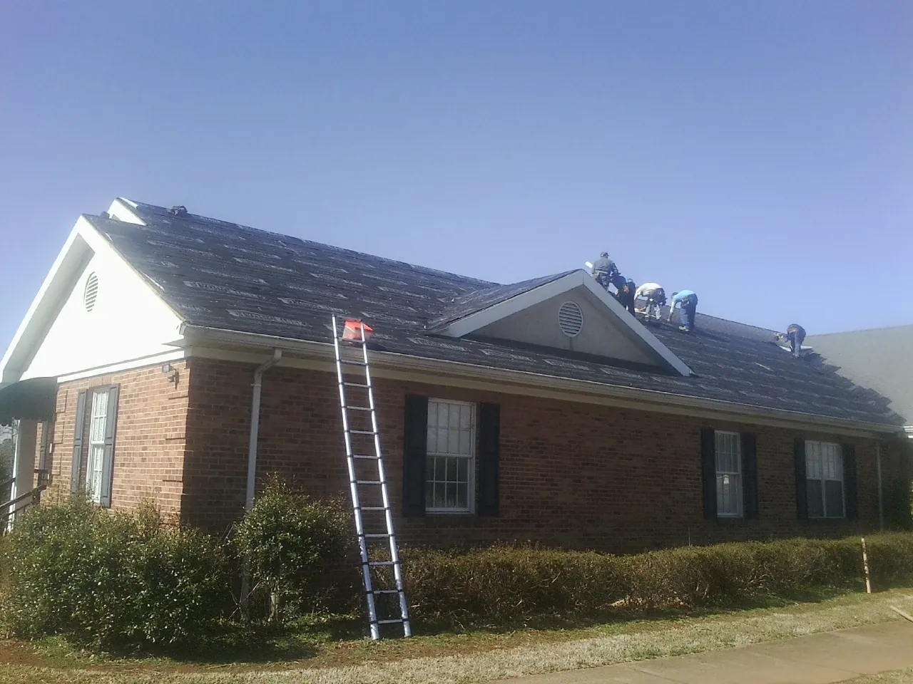 Crew tearing shingles off a brick ranch roof with a ladder set — Emergency Roof Repair work by our crew in Dearborn