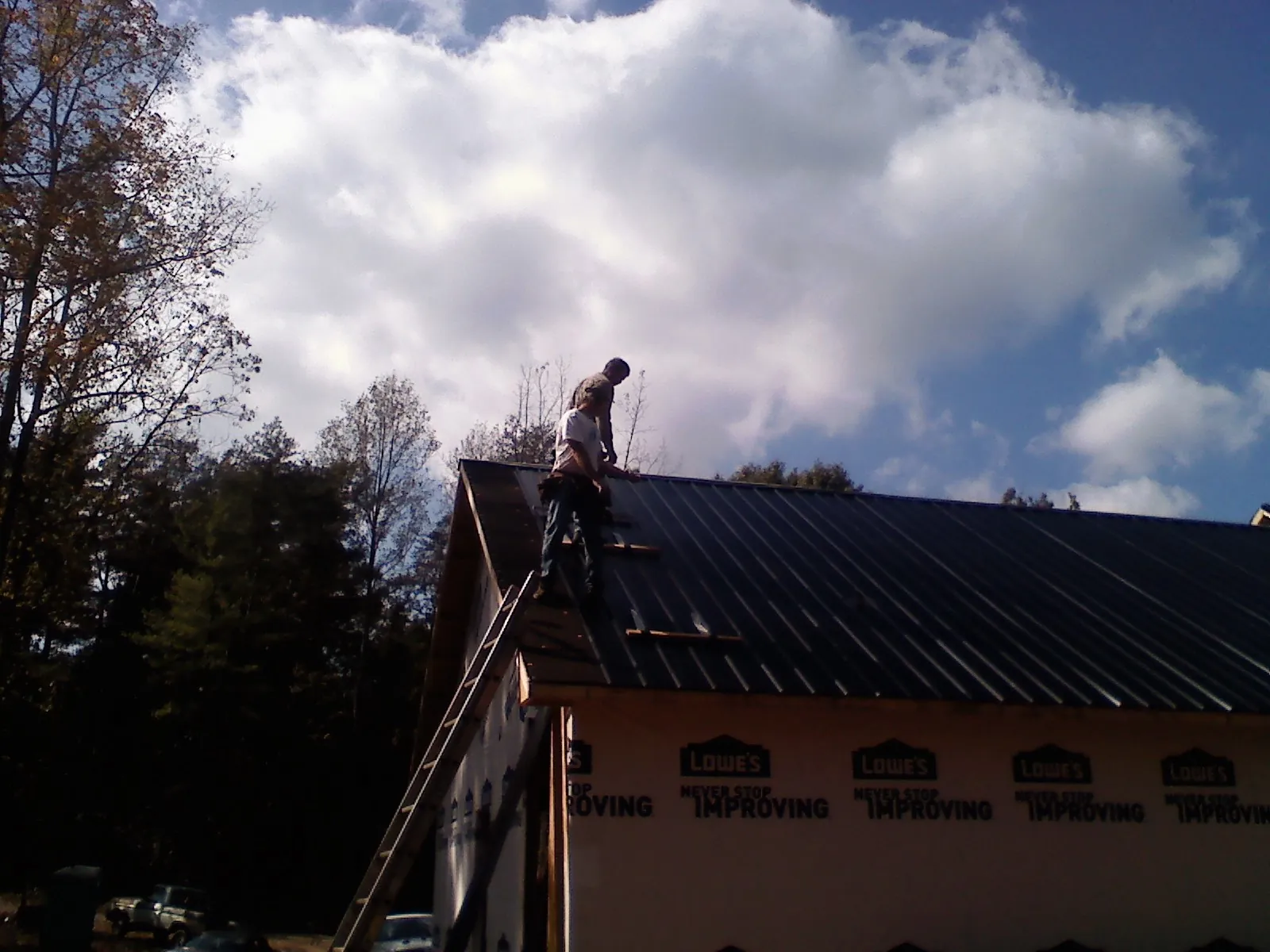 Roofer fastening dark metal panels high against a cloudy sky, from a Roof Inspection job in Dearborn
